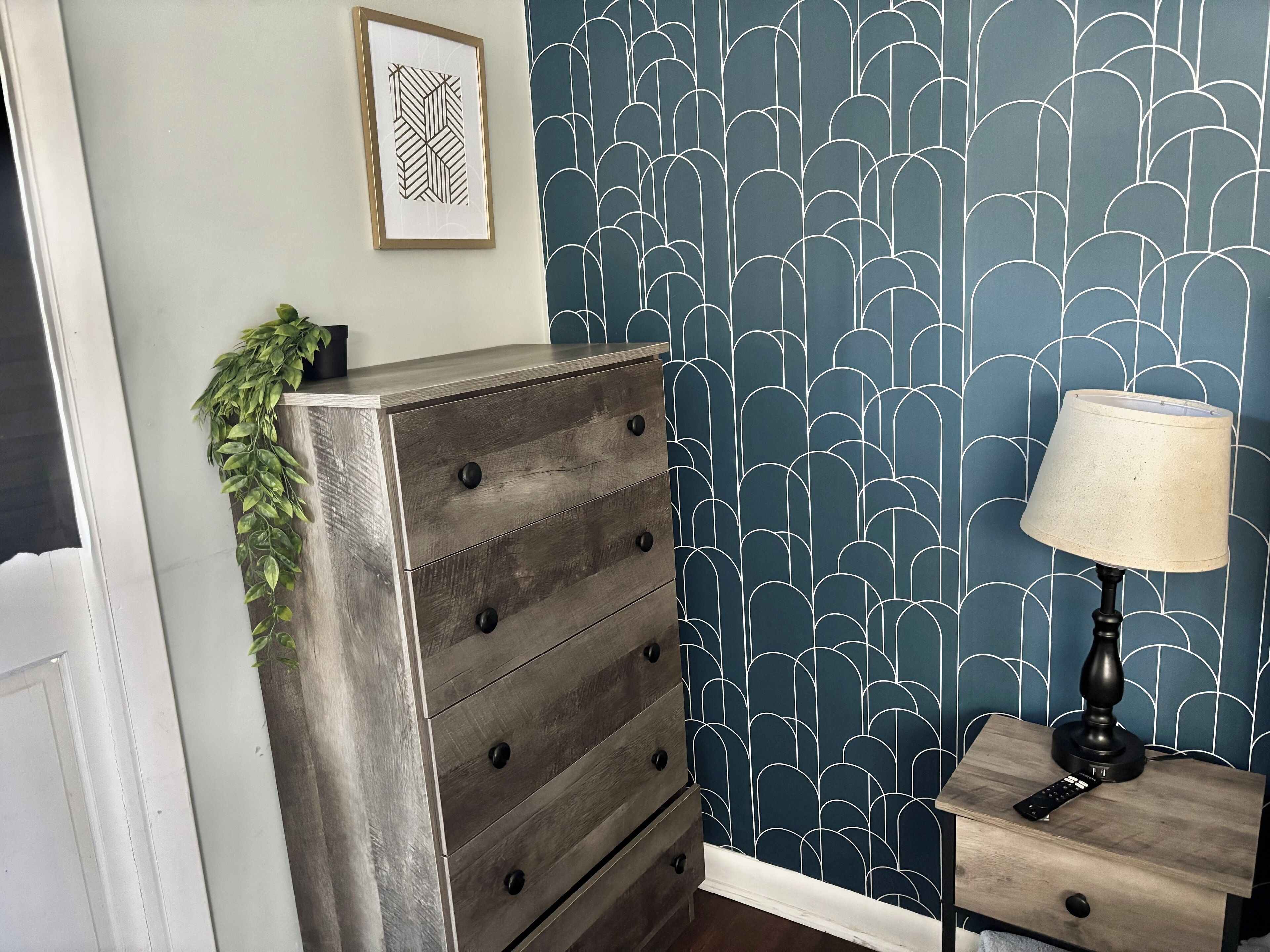 A room with a dresser, a lamp, and a wall with a geometric pattern.