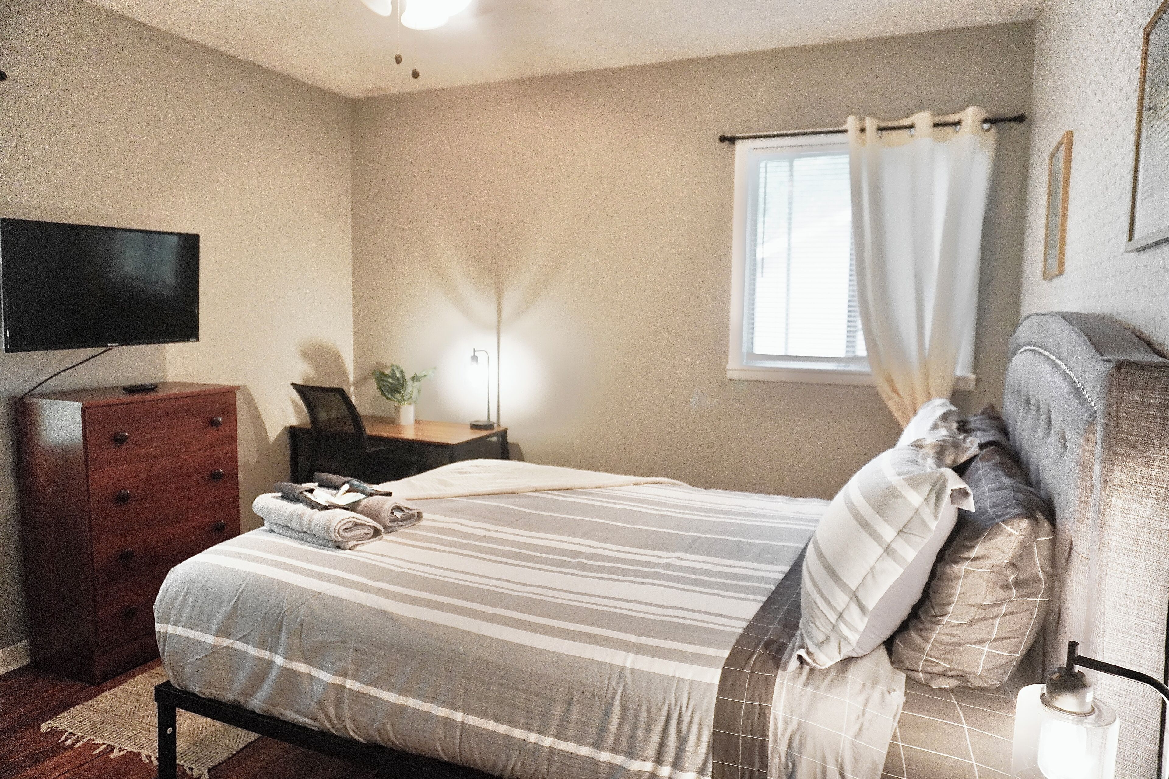 Une chambre à coucher comprenant un lit, une commode, un bureau, une lampe et un téléviseur.