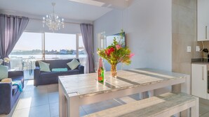 A modern living room with a sofa, a dining table, and a view of the water. - Luxury Riverside Getaway | Balcony | Pool (Velddrif)