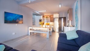 A modern living room with a sofa, a dining table, and a kitchen in the background. - Luxury Riverside Getaway | Balcony | Pool (Velddrif)