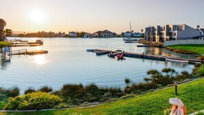 A marina with boats docked, a grassy area, and modern buildings in the background. - Luxury Riverside Getaway | Balcony | Pool (Velddrif)