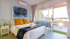 A bedroom with a bed, a nightstand, a painting, and a view of the outdoors. - Luxury Riverside Getaway | Balcony | Pool (Velddrif)