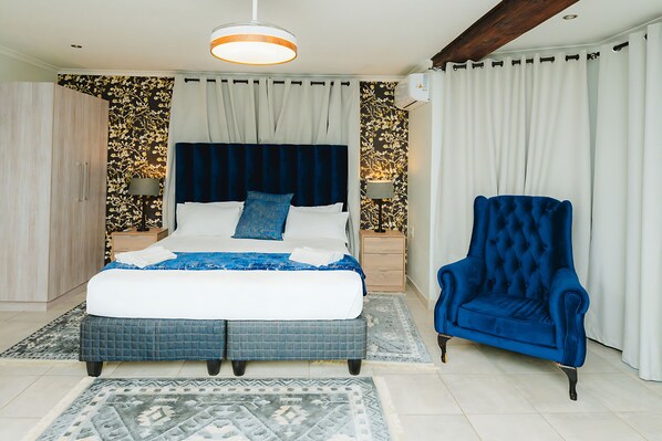 A bedroom with a large bed, a blue armchair, and a patterned rug.