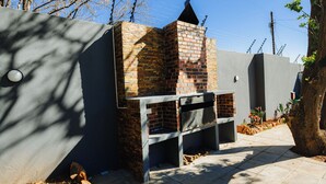 A brick-built outdoor grill with a chimney, set against a grey wall with a tree and power lines in the background. - Mawo Luxury Boutique (Johannesburg)