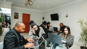 A modern hotel lobby with glass tables, people working on laptops, and a flat-screen TV on the wall. - Mawo Luxury Boutique (Johannesburg)