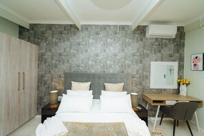 A bedroom with a bed, a desk, a chair, a wardrobe, and a mirror. - Mawo Luxury Boutique (Johannesburg)