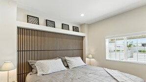 A neatly arranged bedroom with a bed, bedside lamps, and a window with blinds.