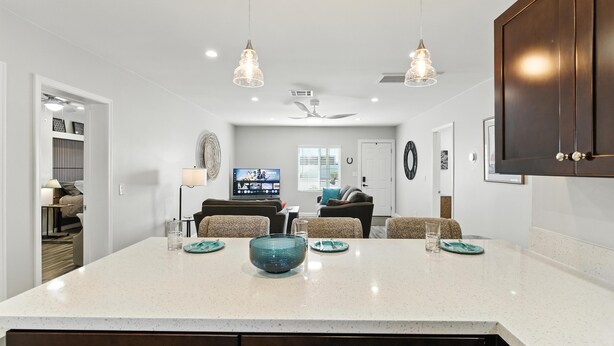 A modern kitchen with a central island, pendant lighting, and a dining area with a TV.