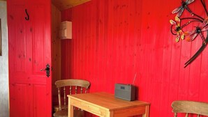 Una habitación con una puerta roja, dos sillas de madera, una mesa de madera y un radio sobre la mesa.