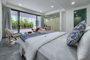 A modern hotel room with a large bed, a rocking chair, a small table, and a view of the outdoors.