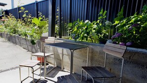 Een terras met metalen stoelen en een tafel, omgeven door een betonnen muur en diverse planten.