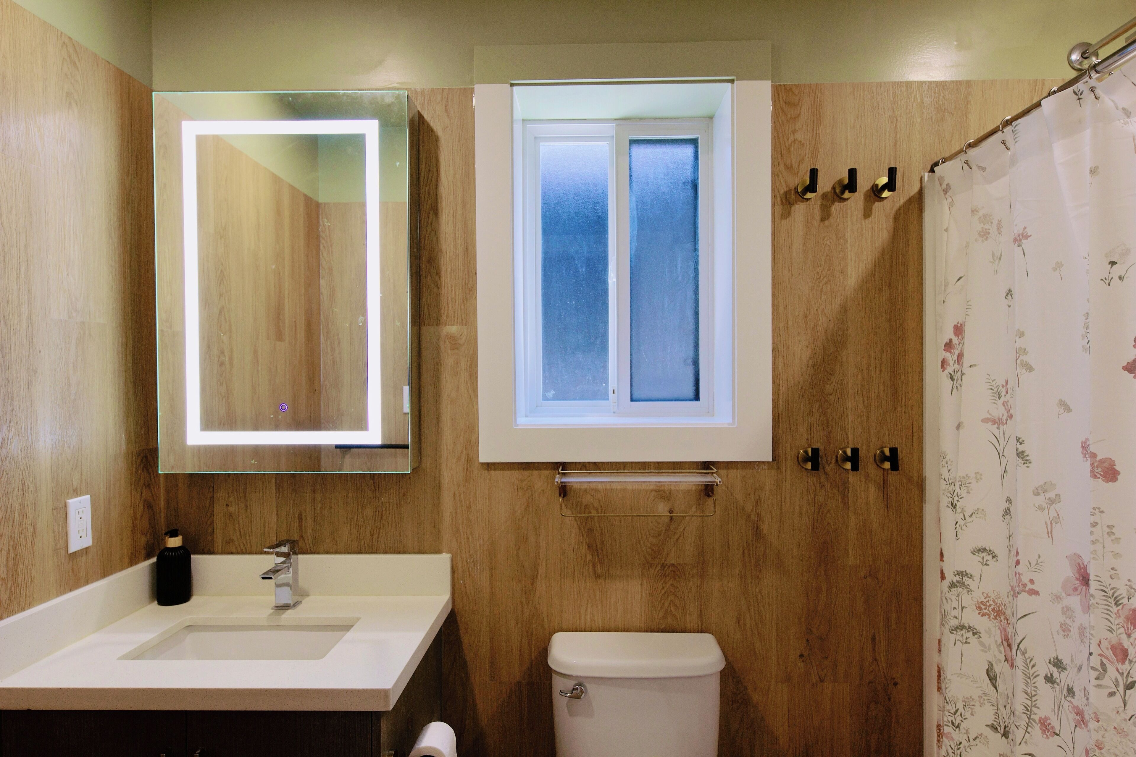 Un bagno con un mobile bagno in legno, uno specchio, una finestra e un water.