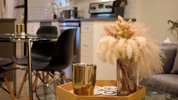 Een moderne keuken met een eethoek, met een glazen tafel, zwarte stoelen en een decoratieve vaas met veren van dodaarsgras.