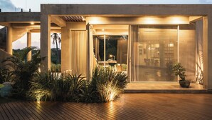 A modern house with a wooden deck, large glass windows, and a well-lit interior. - Kuze House by Alfred in Bali (Canggu)