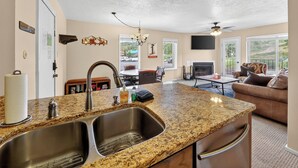 Eine Küche mit Granit Arbeitsplatten, einer Edelstahl-Spüle und einem eingebauten Ofen. Es gibt einen Essbereich mit Tisch und Stühlen sowie ein Wohnzimmer mit einer Couch und einem Kamin.