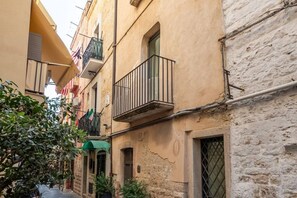 A narrow street with buildings, a balcony with a railing, and a door.