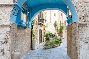 An alleyway with a blue archway, a sign reading 'Corte Carducci,' and potted plants.