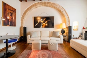 A living room with a white sofa, two ottomans, a patterned rug, a painting, a lamp, and a fireplace.