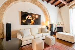 Ein Wohnzimmer mit einem weißen Sofa, Poufs, einem Couchtisch, einem Kamin und einem steinernen Bogen.