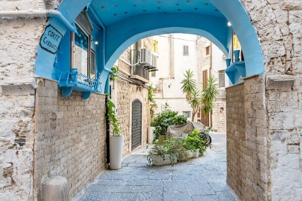 An alleyway with a blue archway, a sign reading 'Corte Carducci,' and potted plants.