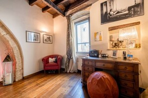 A room with a wooden floor, a red chair, a wooden desk with drawers, a lamp, and a window with curtains.