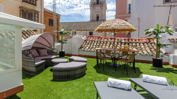 A rooftop patio with outdoor furniture, a thatched umbrella, and a view of a historic building with a bell tower.