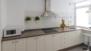 A modern kitchen with white cabinets, a stainless steel range hood, a microwave, a fruit bowl, and a window providing natural light.