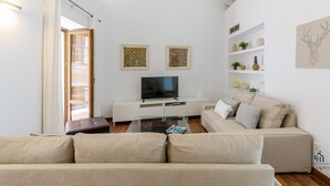 A modern living room with a high ceiling, a flat-screen TV, a sofa, and decorative items on shelves.