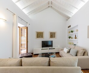 Un salón moderno con techo alto, televisor de pantalla plana, sofá y objetos decorativos en estanterías.