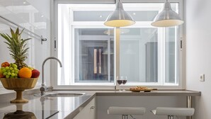A modern kitchen with a large window, a fruit bowl, two pendant lights, and a bar area.