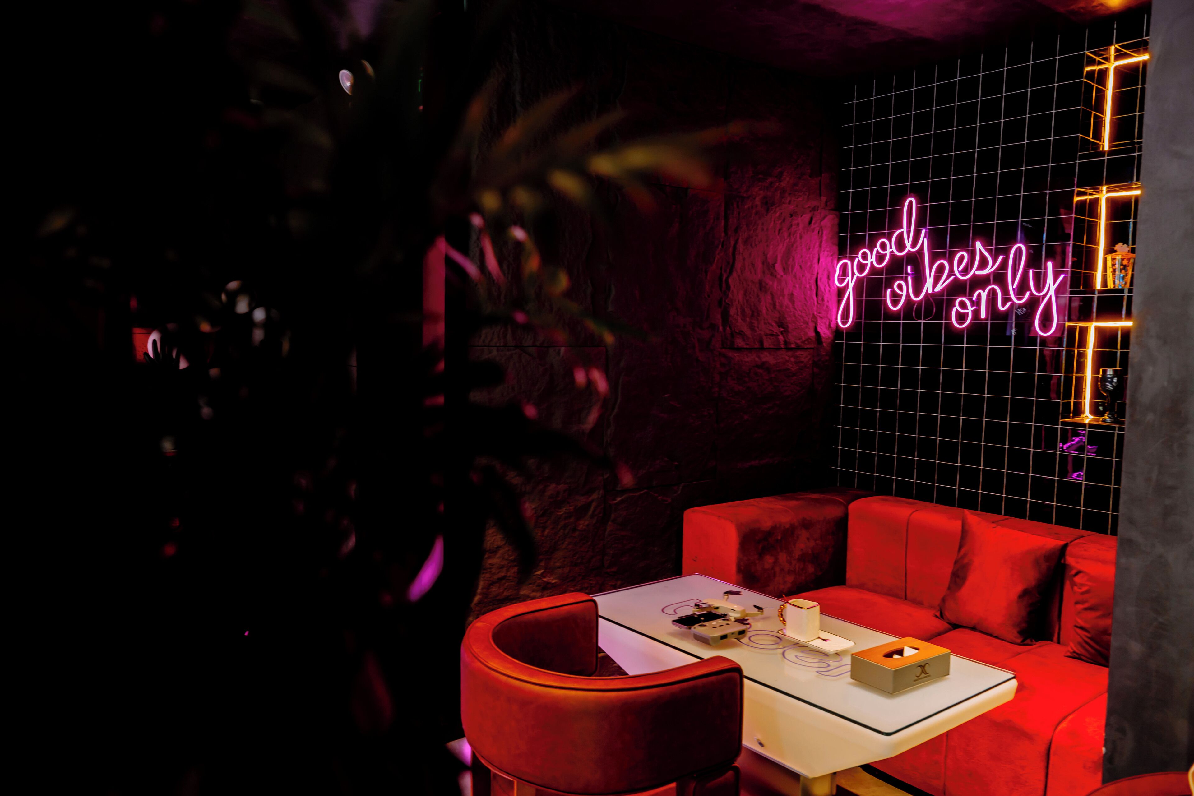 Une pièce faiblement éclairée, avec un canapé rouge, une petite table et un panneau néon sur lequel on peut lire : « ambiance positive uniquement ».