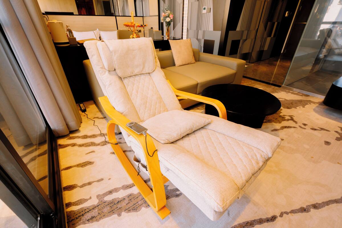 A modern living room with a large beige sofa, a yellow armchair with a quilted seat, and a black ottoman.