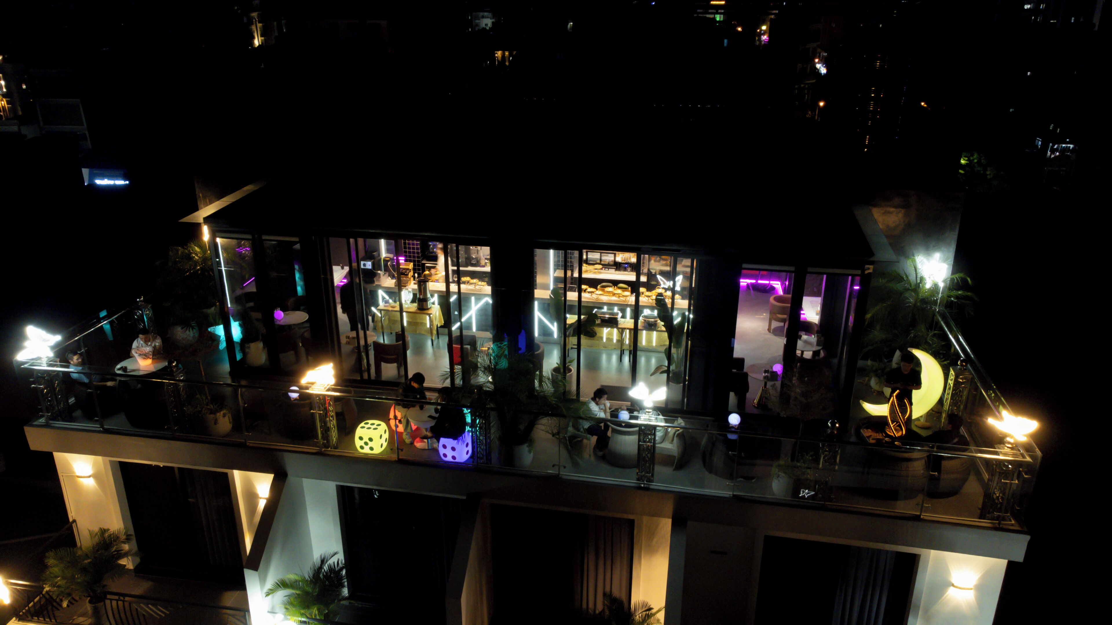 A modern building with a glass facade, interior lighting, and outdoor seating areas.
