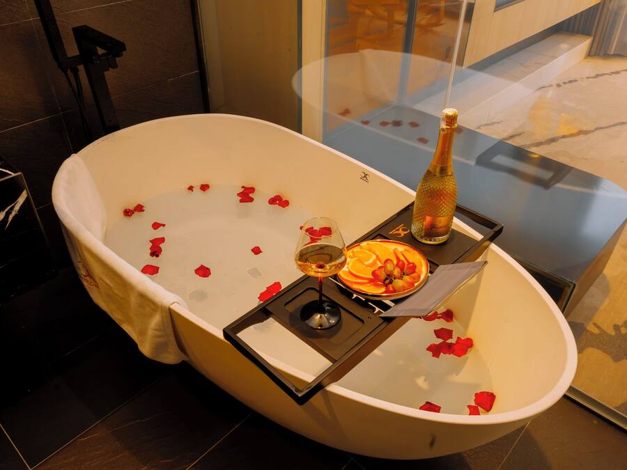 Una bañera con pétalos de rosa, una botella de champán y una copa de vino.