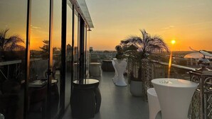A balcony with a view of the sunset, featuring a glass railing, white furniture, and potted plants. - X-Digital Hotel (Kinh Bac)