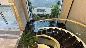 A modern interior with a glass staircase, a potted plant, and a view through a large window. - X-Digital Hotel (Kinh Bac)