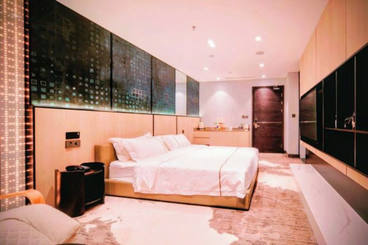 A modern bedroom with a large bed, a vanity with a mirror, and a TV mounted on the wall.