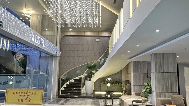 A modern hotel lobby with a curved staircase, a reception desk, and a decorative light installation. - X-Digital Hotel (Kinh Bac)