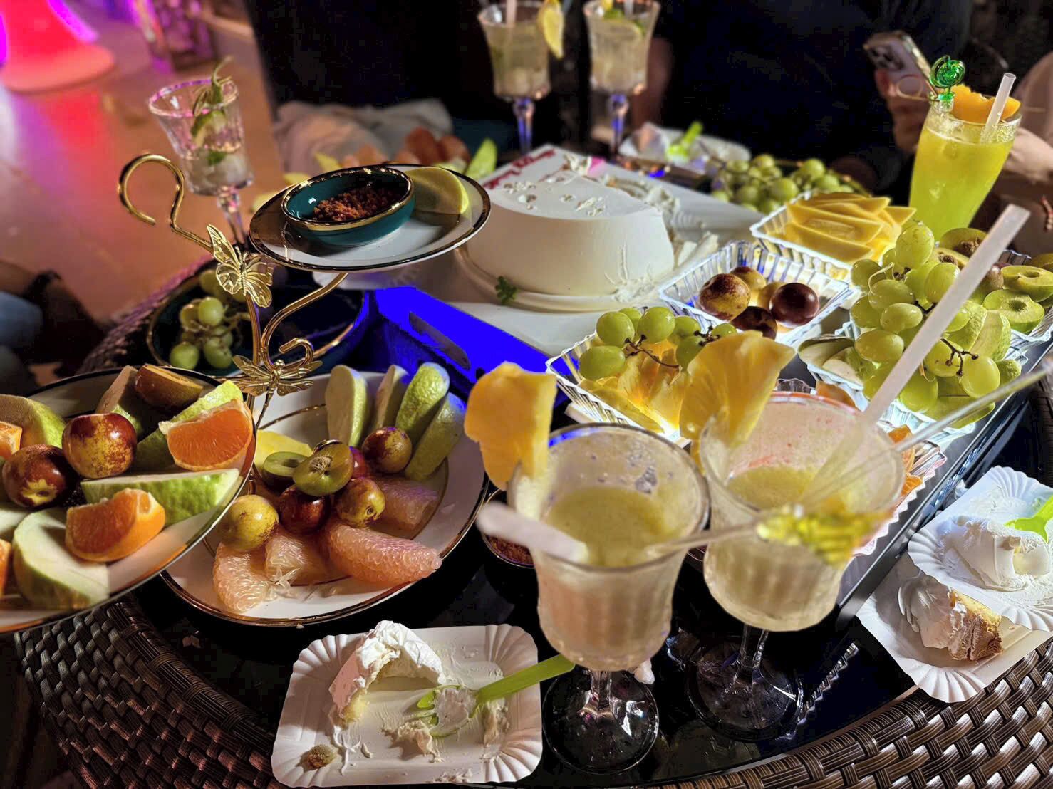 A table with various fruits, cheeses, and drinks, likely set up for a gathering or event.