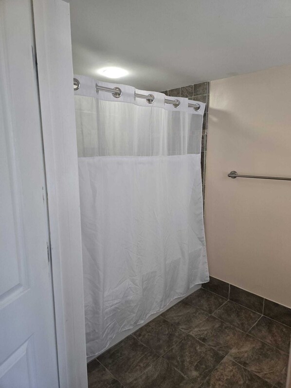 Un baño con cortina de ducha blanca, toallero y suelo de baldosas.