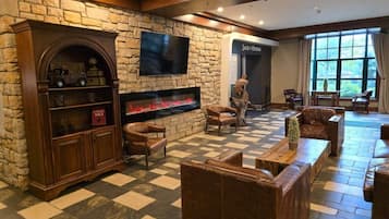 A hotel lobby with a stone wall, a fireplace, leather sofas, and a television.