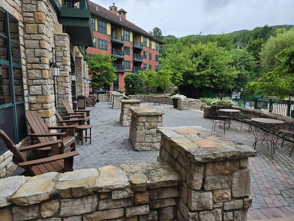 An outdoor patio with stone walls, wooden chairs, and tables.