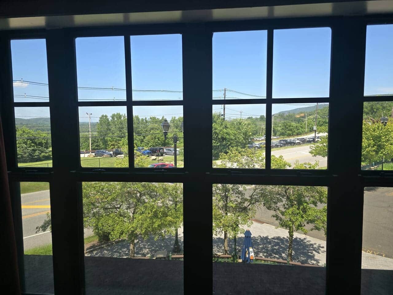 Vista per una finestra amb cel blau, arbres i un aparcament.