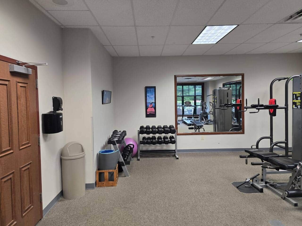 A gym with exercise equipment, a mirror, and a door on the left.
