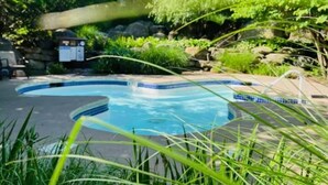 A swimming pool with a curved edge, surrounded by lush greenery and rocks.