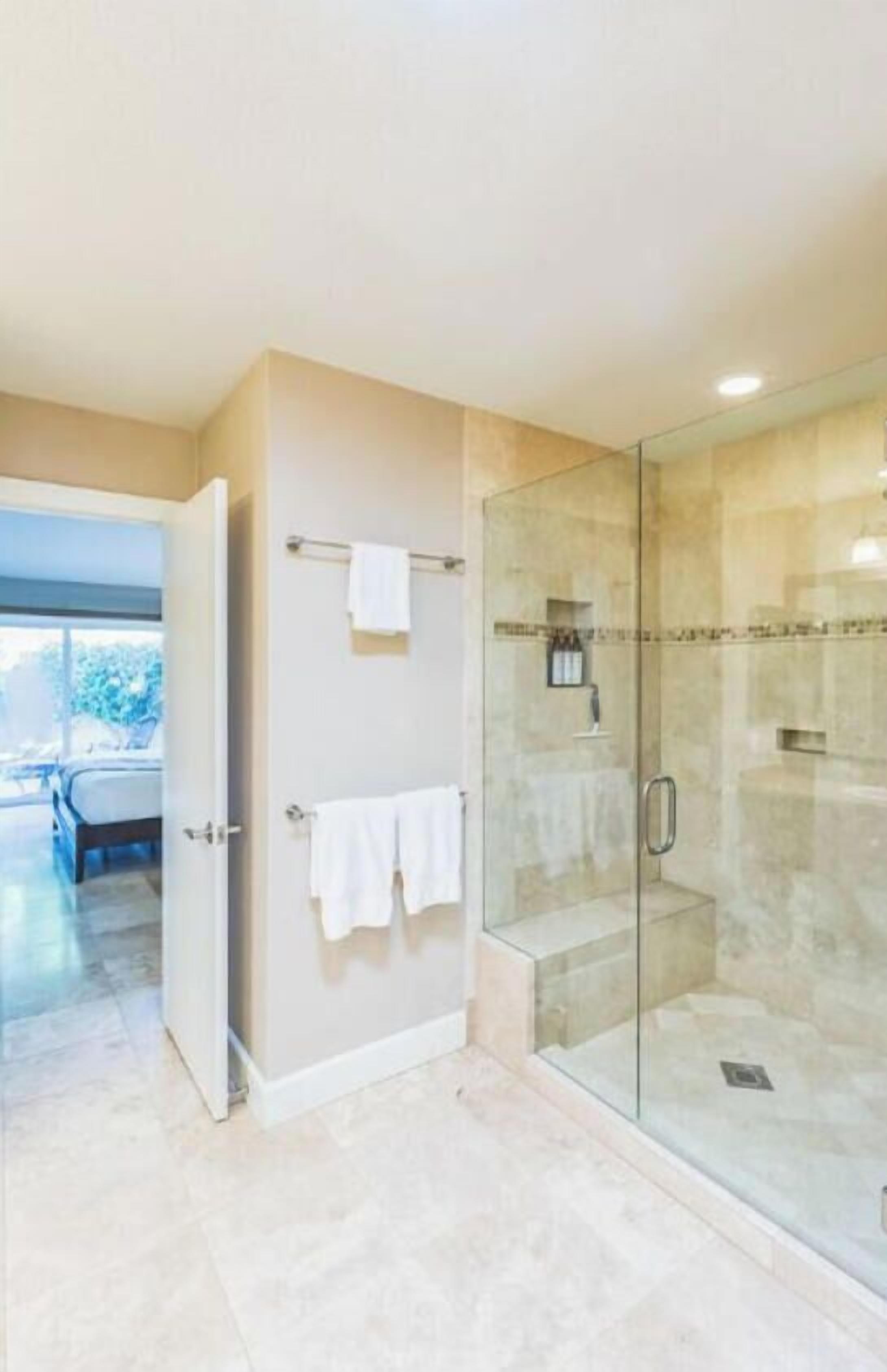 A modern bathroom with a glass shower enclosure, a visible towel rack, and a door leading to another room.