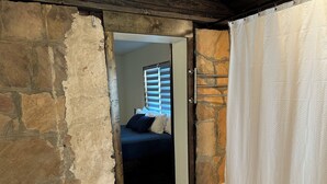 Un petit couloir étroit mène à une chambre à coucher qui contient un lit, une fenêtre avec des stores et un rideau blanc.