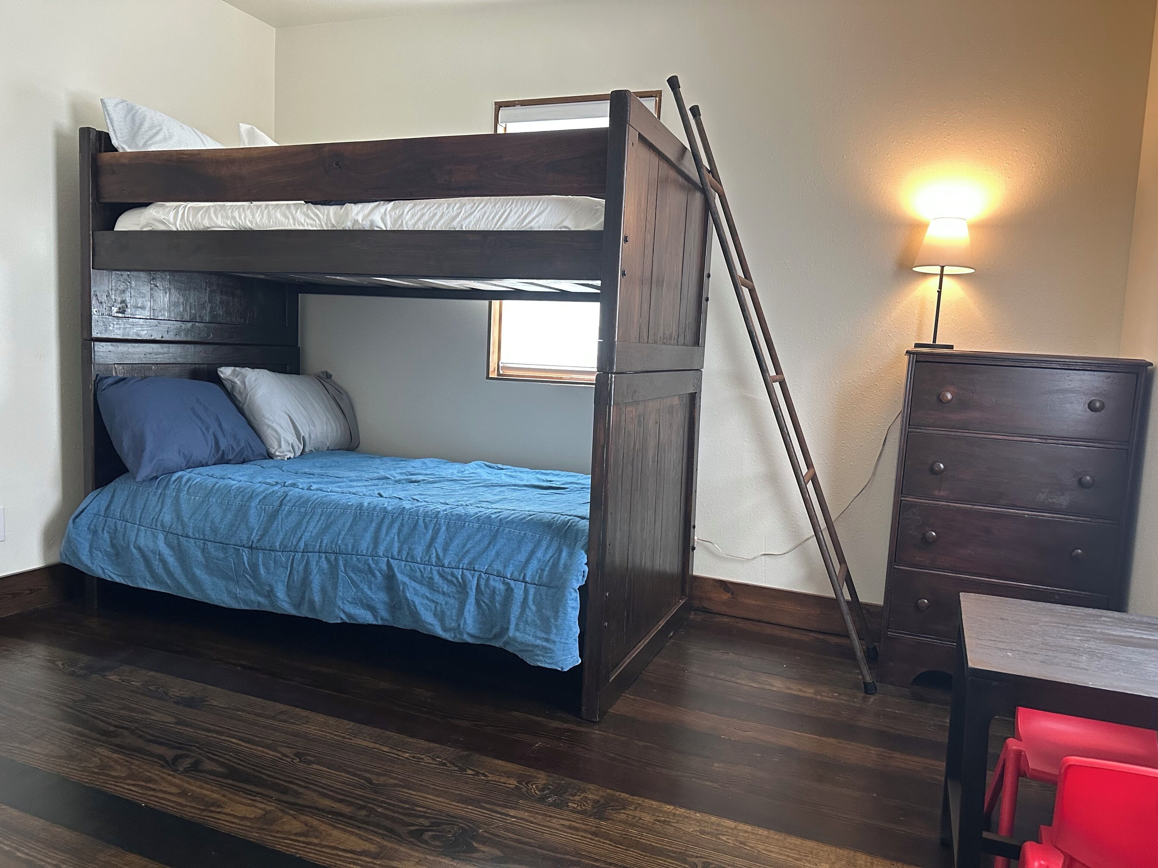 A bunk bed with a ladder, a dresser, and a desk with a chair.
