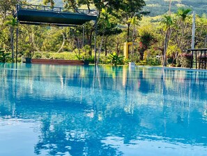 A clear blue pool with a wooden deck and a bridge, surrounded by lush greenery and trees. - Thisak Resort Cheung Phnom Kulen (Svay Leu)