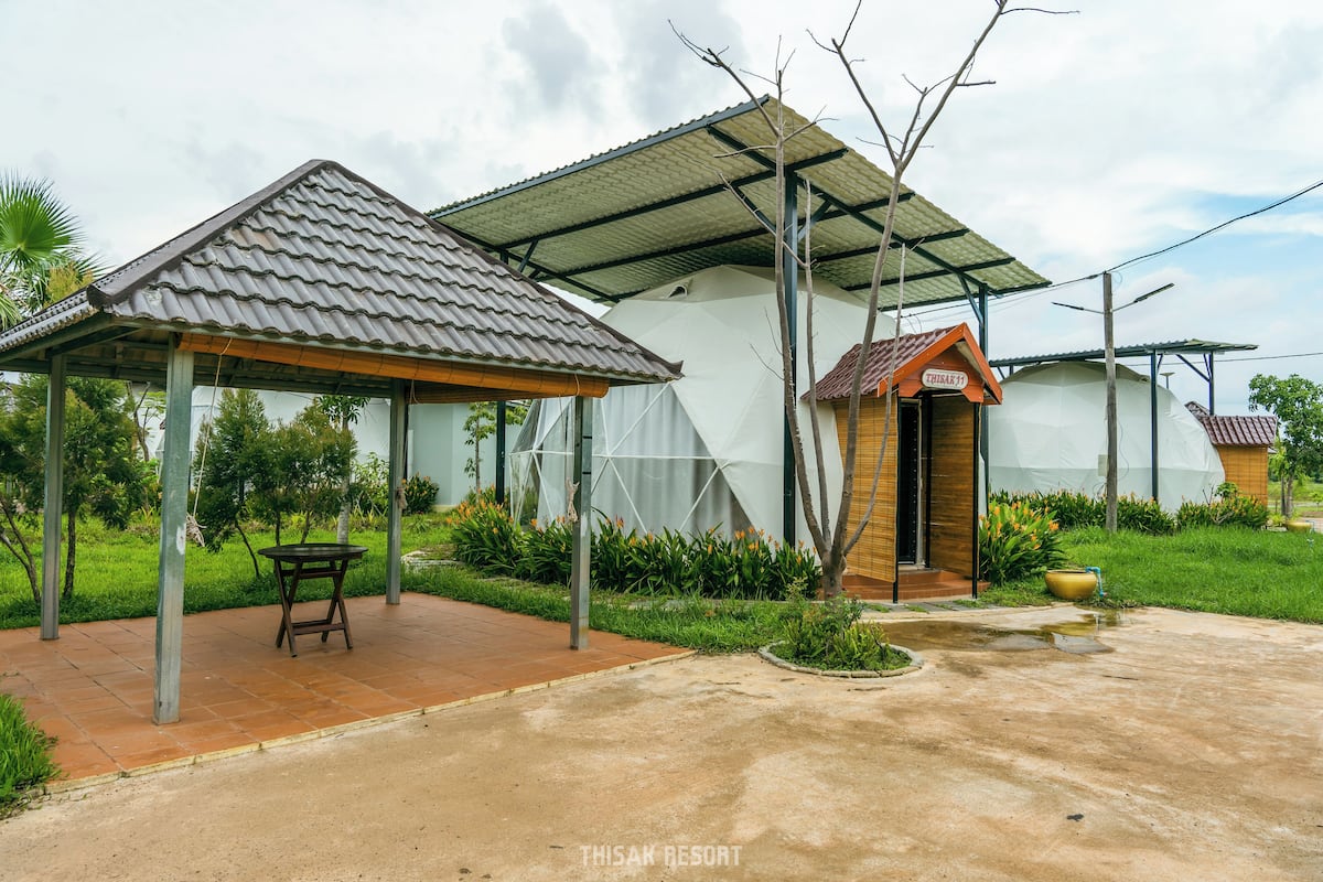 Un complexe hôtelier doté d’un espace extérieur couvert avec des sièges, d’un bâtiment avec un toit en tuiles et d’une enseigne indiquant la présence d’un restaurant.